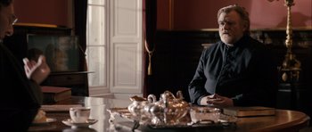 Movie still from “Calvary” (2014), directed by John Michael McDonagh – A man sitting in front of a table with a tray of silverware; Medium shot, Over the shoulder angle