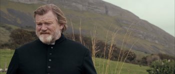 Movie still from “Calvary” (2014), directed by John Michael McDonagh – An older man with a beard standing next to a field; Close Up shot, Over the shoulder angle