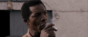 Movie still from “Calvary” (2014), directed by John Michael McDonagh – A man smoking a cigarette in front of a building; Close Up shot, Low angle