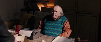 Movie still from “Calvary” (2014), directed by John Michael McDonagh – An older man sitting at a table with papers; Medium shot, Over the shoulder angle