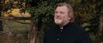 Movie still from “Calvary” (2014), directed by John Michael McDonagh – A man with long hair and a beard wearing a priest's outfit; Medium shot, Low angle