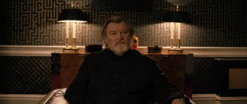 Movie still from “Calvary” (2014), directed by John Michael McDonagh – A man with a beard is sitting in a chair; Medium shot, Low angle