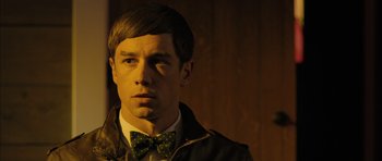Movie still from “Calvary” (2014), directed by John Michael McDonagh – A man wearing a green bow tie in a dark room; Close Up shot, Over the shoulder angle