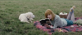 Movie still from “Calvary” (2014), directed by John Michael McDonagh – A woman reading a book while laying in the grass with a dog; Medium shot, High angle