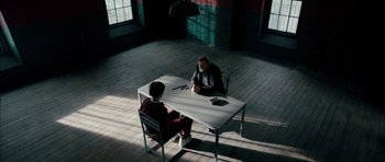 Movie still from “Calvary” (2014), directed by John Michael McDonagh – Two people sitting at a white table in a room; Wide shot, High angle