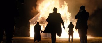 Movie still from “Calvary” (2014), directed by John Michael McDonagh – A group of people standing in front of a house on fire at night; Wide shot, Low angle