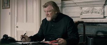 Movie still from “Calvary” (2014), directed by John Michael McDonagh – An older man sitting at a table reading a book; Medium shot, Low angle