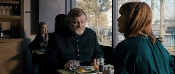 Movie still from “Calvary” (2014), directed by John Michael McDonagh – An older man sitting at a table with a plate of food; Medium shot, Over the shoulder angle