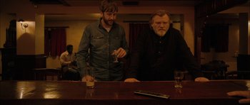 Movie still from “Calvary” (2014), directed by John Michael McDonagh – Two men standing at a bar with a drink in their hand; Medium shot, Low angle