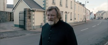 Movie still from “Calvary” (2014), directed by John Michael McDonagh – An older man with long hair and a long beard walking down the street; Medium shot, Over the shoulder angle