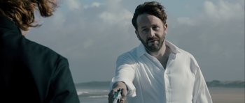 Movie still from “Calvary” (2014), directed by John Michael McDonagh – A man in a white shirt holding a gun in his right hand; Close Up shot, Over the shoulder angle