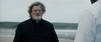 Movie still from “Calvary” (2014), directed by John Michael McDonagh – A man with a beard wearing a priest's outfit; Medium shot, Over the shoulder angle