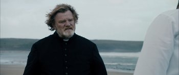 Movie still from “Calvary” (2014), directed by John Michael McDonagh – A man with long hair and a beard wearing a priest's outfit; Medium shot, Over the shoulder angle