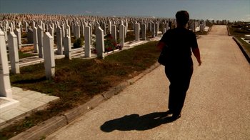 Movie still from “Cameraperson” (2016), directed by Kirsten Johnson – A person walking down a road near a cemetery; Extreme Wide shot, High angle