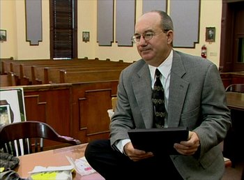 Movie still from “Cameraperson” (2016), directed by Kirsten Johnson – A man in a suit and tie holding a tablet; Medium shot, High angle