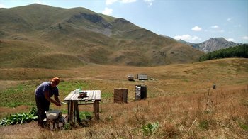 Movie still from “Cameraperson” (2016), directed by Kirsten Johnson – A man standing next to a table in the middle of a field; Extreme Wide shot, High angle