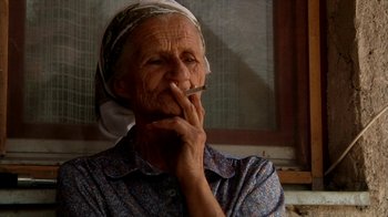Movie still from “Cameraperson” (2016), directed by Kirsten Johnson – An older woman smoking a cigarette in front of a window; Close Up shot, Low angle