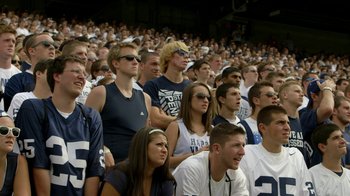 Movie still from “Cameraperson” (2016), directed by Kirsten Johnson – A group of people sitting in a stadium watching a football game; Medium shot, High angle