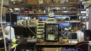 Movie still from “Cameraperson” (2016), directed by Kirsten Johnson – A room filled with lots of computer equipment and wires; Wide shot, High angle