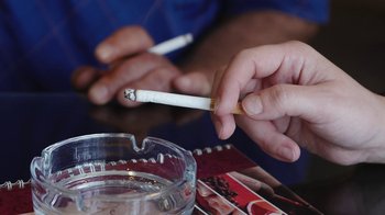 Movie still from “Cameraperson” (2016), directed by Kirsten Johnson – A person is holding a cigarette in their hand; Extreme Close Up shot, Overhead angle