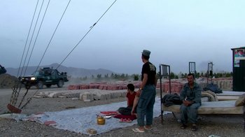 Movie still from “Cameraperson” (2016), directed by Kirsten Johnson – A group of people sitting on the ground near a road; Wide shot, Low angle