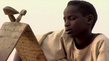 Movie still from “Cameraperson” (2016), directed by Kirsten Johnson – A young man reading a book in front of a sky background; Close Up shot, Low angle