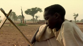 Movie still from “Cameraperson” (2016), directed by Kirsten Johnson – A young boy holding a stick in a field; Close Up shot, Low angle