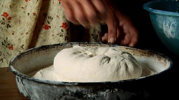 Movie still from “Cameraperson” (2016), directed by Kirsten Johnson – A person is making bread dough in a pan; Extreme Close Up shot, Overhead angle