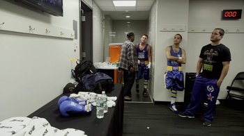 Movie still from “Cameraperson” (2016), directed by Kirsten Johnson – A group of men standing around in a room; Wide shot, High angle