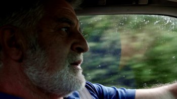 Movie still from “Cameraperson” (2016), directed by Kirsten Johnson – An older man with a beard driving in the rain; Close Up shot, Over the shoulder angle