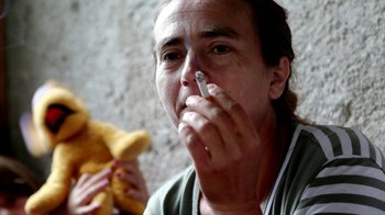 Movie still from “Cameraperson” (2016), directed by Kirsten Johnson – A woman smoking a cigarette while holding a teddy bear; Extreme Close Up shot, High angle