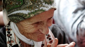 Movie still from “Cameraperson” (2016), directed by Kirsten Johnson – An old woman with a head scarf is looking at the camera; Close Up shot, High angle
