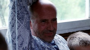 Movie still from “Cameraperson” (2016), directed by Kirsten Johnson – A man with a shaved head sitting in front of a window; Close Up shot, High angle
