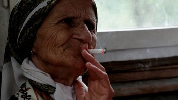 Movie still from “Cameraperson” (2016), directed by Kirsten Johnson – An older woman smoking a cigarette in front of a window; Close Up shot, Low angle
