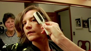 Movie still from “Cameraperson” (2016), directed by Kirsten Johnson – A woman holding a hair brush in front of a mirror; Close Up shot, Over the shoulder angle