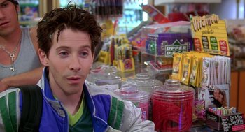 Movie still from “Can't Hardly Wait” (1998), directed by Deborah Kaplan – A man sitting in front of a counter filled with candy; Close Up shot, Over the shoulder angle