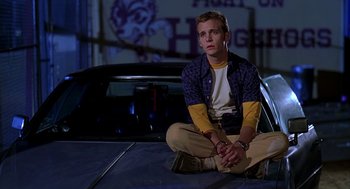Movie still from “Can't Hardly Wait” (1998), directed by Deborah Kaplan – A man sitting on the hood of a car at night; Medium shot, Low angle