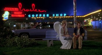 Movie still from “Can't Hardly Wait” (1998), directed by Deborah Kaplan – Two people sitting on a park bench in front of a coffee shop at night; Wide shot, Over the shoulder angle