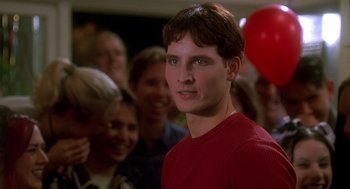 Movie still from “Can't Hardly Wait” (1998), directed by Deborah Kaplan – A man in a red shirt is smiling for the camera; Close Up shot, Over the shoulder angle