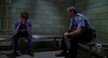 Movie still from “Can't Hardly Wait” (1998), directed by Deborah Kaplan – A police officer sitting on a bench talking on a cell phone; Medium shot, Over the shoulder angle