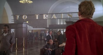 Movie still from “Can't Hardly Wait” (1998), directed by Deborah Kaplan – A man sitting in a chair in a train station; Medium shot, Over the shoulder angle