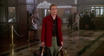 Movie still from “Can't Hardly Wait” (1998), directed by Deborah Kaplan – A man in a red jacket is holding some bags; Medium shot, Low angle