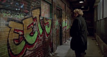 Movie still from “Candyman” (1992), directed by Bernard Rose – A person standing in front of a brick wall with graffiti on it; Wide shot, Over the shoulder angle