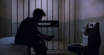 Movie still from “Candyman” (1992), directed by Bernard Rose – A man sitting in a jail cell holding a knife; Wide shot, High angle