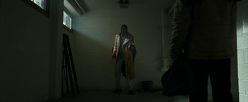 Movie still from “Candyman” (2021), directed by Nia DaCosta – A man wearing a trench coat in a dark room; Medium shot, Low angle