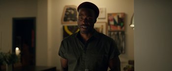 Movie still from “Candyman” (2021), directed by Nia DaCosta – A man in a hat is standing in a room; Medium shot, Over the shoulder angle