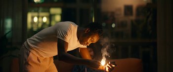 Movie still from “Candyman” (2021), directed by Nia DaCosta – A man holding a cell phone while standing in front of a fire; Close Up shot, Low angle