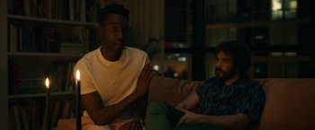 Movie still from “Candyman” (2021), directed by Nia DaCosta – Two men sitting on a couch in a living room at night; Medium shot, Over the shoulder angle