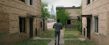 Movie still from “Candyman” (2021), directed by Nia DaCosta – A man walking down a sidewalk near a building; Wide shot, Over the shoulder angle