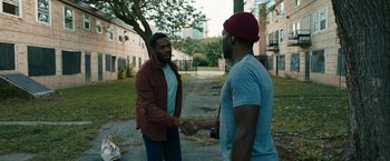 Movie still from “Candyman” (2021), directed by Nia DaCosta – Two men are shaking hands in an urban setting; Medium shot, Over the shoulder angle